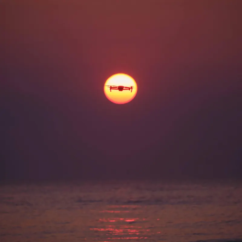 Silhouet van een drone voor de ondergaande zon boven zee