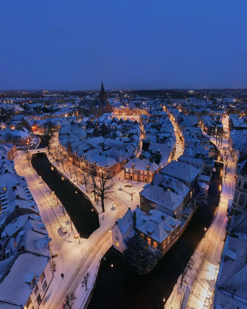 Besneeuwde binnenstad met gracht in het blauwe uur, vanuit de lucht